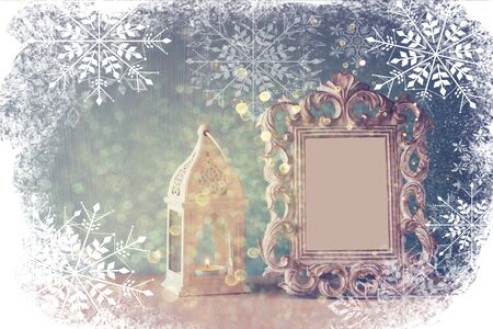 abstract image of vintage antique classical frame and old lantern on wooden table with snowflakes overlayの写真素材