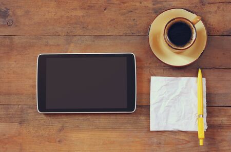 top view image of tablet device, coffee and paper note over wooden background
