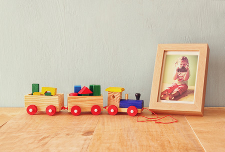 Wooden toy train over wooden table next to photo frame with old kid photography. retro filtered imageの写真素材