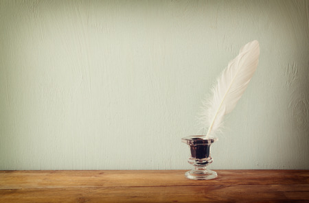 photo of white Feather and inkwell on old wooden table. retro filtered imageの写真素材