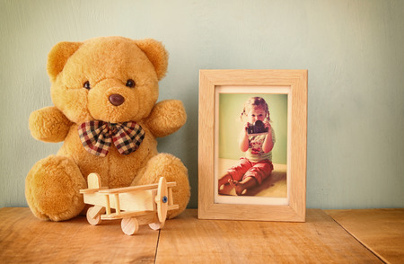 wooden airplane toy and teddy bear over wood table next to photo frame with kid's old photography. retro filtered imageの写真素材