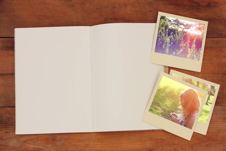 open blank notebook and old travel polaroid photographs over wooden table. ready for mockup. retro filtered imageの写真素材