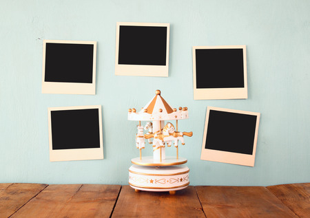 blank instant photos hang over wooden textured background next to vintage white carousel horsesの写真素材