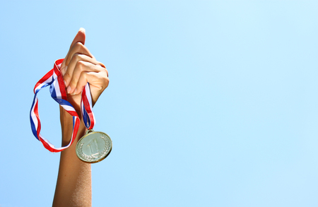 woman hand raised, holding gold medal against skyl. award and victory concept. selective focus. retro style image.の写真素材