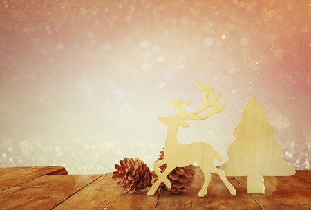abstract image of wooden decorative christmas tree, reindeer and pine cones on wooden table and christmas holiday bokeh lightsの写真素材