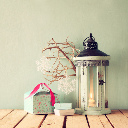 white wooden vintage lantern with burning candle christmas gifts and tree branches on wooden table. retro filtered imageの写真素材