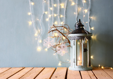 low key white wooden vintage lantern with burning candle and tree branches on wooden table. retro filtered imageの写真素材