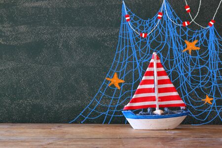 photo of wooden sailing boat in front of chaklboard with nautical illustrations.の写真素材