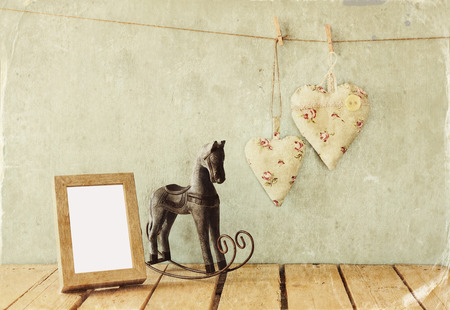 vintage rocking horse next to fabric hearts hanging on the rope on wooden floor and blank photo frame. retro filtered imageの写真素材