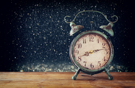 image of vintage alarm clock on wooden table in front of magical glitter silver and black lights background. retro filtered