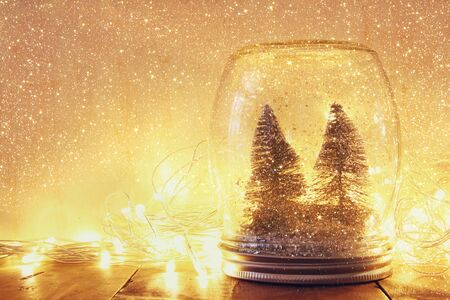 low key and vintage filtered image of christmas trees in mason jar with garland warm lights and glitter overlay. selective focusの写真素材