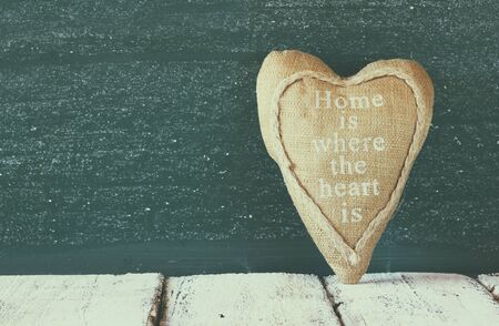 image of vintage fabric heart on wooden table in front of blackboard. faded retro style filterの写真素材