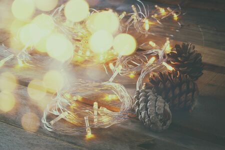 double exposure photo of pine cones next to gold garland lights on wooden background. copy space