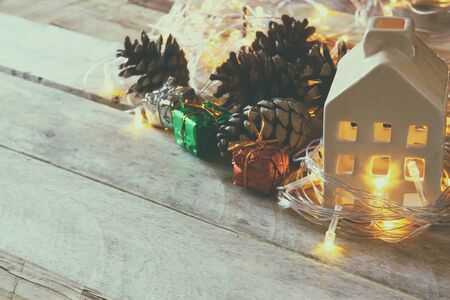 pine cones and decorative wooden house next to gold garland lights on wooden background. copy spaceの写真素材