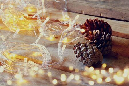 pine cones next to gold garland lights on wooden background. copy spaceの写真素材