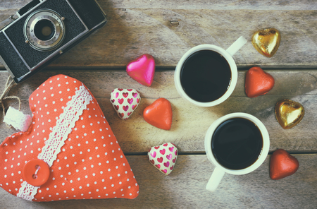 top view image of colorful heart shape chocolates, fabric heart, vintage photo camera and cup of coffee on wooden table. valentine's day celebration concept. retro filtered and tonedの写真素材