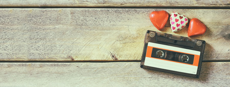 website banner image of colorful heart shape chocolates and audio cassette on wooden table. valentine's day celebration concept. retro toned and filteredの写真素材