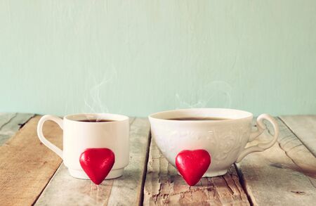 image of two red heart shape chocolates and couple cups of coffee on wooden table. valentine's day celebration concept. vintage filteredの写真素材