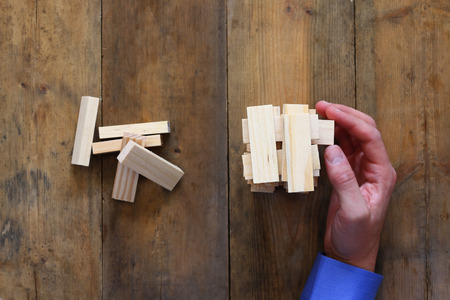 top view of male hand placing wooden block on a tower. planing and strategy concept