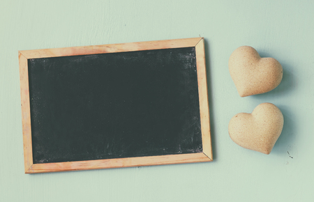 top view image of wooden hearts next to blackboard on wooden light blue background. valentine's day celebration concept. vintage filtered and tonedの写真素材