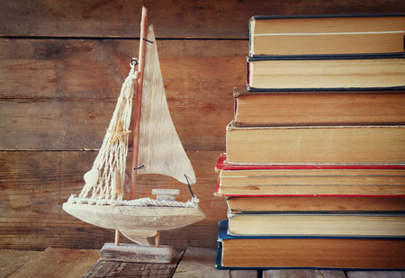 stack of old books next to decorative sailing boat wooden table. vintage filtered imageの写真素材