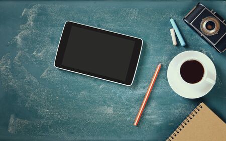 top view image of tablet, cup of coffee and photo camera over blackboard background