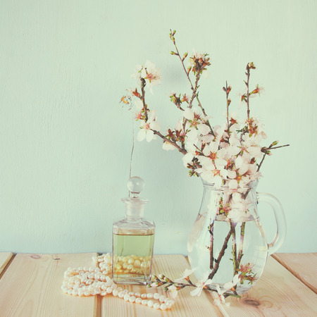 fresh vintage perfume bottle next to white spring flowers on wooden table. vintage filtered imageの写真素材