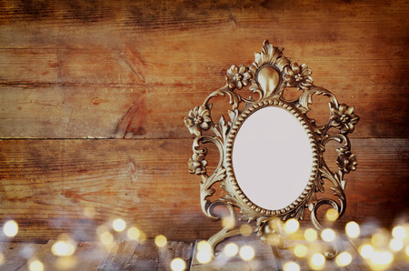 double exposure image of Antique blank victorian style frame and gold lights on wooden table. vintage filtered image. template, ready to put photographyの写真素材