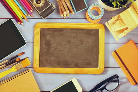 top view photo of blank blackboard, old camera and school supplies on wooden table. vintage filtered