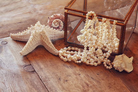 image of white pearls necklace and seashells on old grunge wooden table. vintage filteredの写真素材