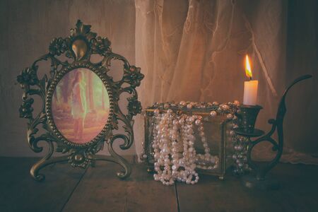low key image of vintage frame with old photo, pearls and burning candle on wooden table. vintage filtered and tonedの写真素材