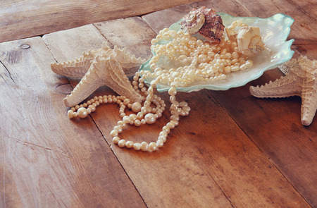 image of white pearls necklace and seashells on old grunge wooden table. vintage filtered