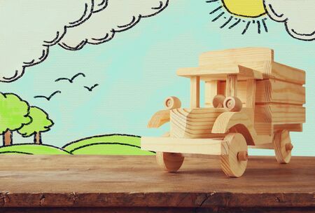 photo of wooden toy car over wooden table and counrtside landscape sketch background. travel and and vacation conceptの写真素材