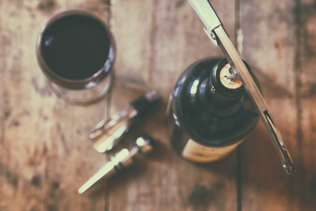 top view image of red wine bottle and corkscrew over wooden table. retro style image selective focus.の写真素材