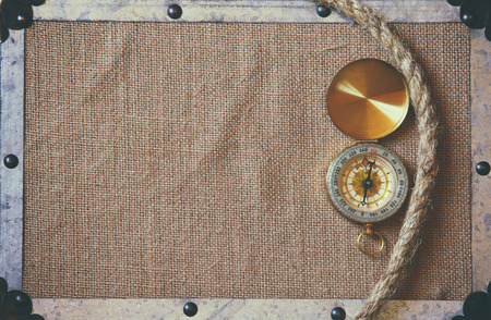 top view of compass and a traveler rope on burlap canvas fabric background with metal frame. explorer and adventure concept. vintage filtered and toned imageの写真素材