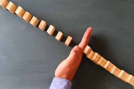a male hand stopping the domino effect. retro style image. executive and risk control concept