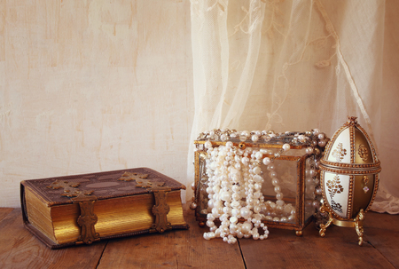 image of white pearls necklace and old book on old grunge wooden table. vintage filteredの写真素材
