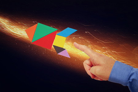 man's hand pointing at rocket made from square tangram puzzle, abstract space background