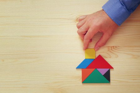 man's hand pointing at house made from tangram puzzle over wooden tableの写真素材