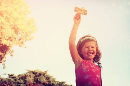 cute little girl holding wooden toy airplane against the sky. retro filtered imageの写真素材