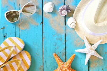 top view of nautical concept with fedora hat, sunglasses, flip flops and seashells on aqua wooden...