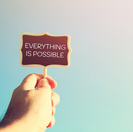man's hand holding the empty wooden sign with quote: EVERYTHING IS POASSIBLE, against the blue skyの写真素材