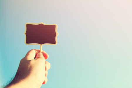 man's hand holding the empty wooden sign against the blue skyの写真素材