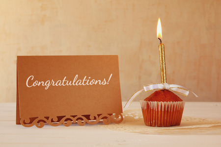 Birthday concept with cupcake and candle next to greeting card on wooden tableの写真素材