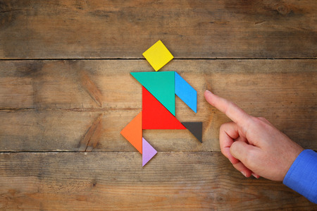 man's hand pointing at running man made from square tangram puzzle, wooden backgroundの写真素材