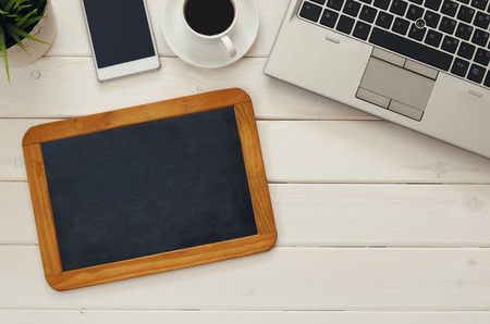 Top view of laptop, empty blackboard, cellphone and cup of coffee over wooden desk