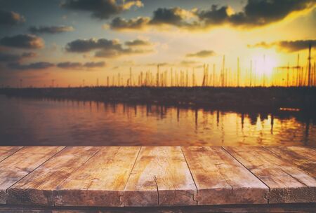 Image of wooden table in front of abstract blurred background of marine view during sunsetの写真素材