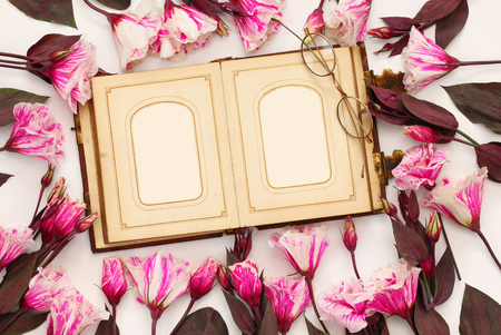 Top view of beautiful pink flowers and old empty photo album on white backgroundの写真素材