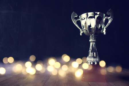 low key image of trophy over wooden table and dark background, with abstract shiny lights