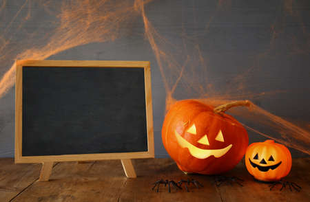 Halloween holiday concept. Cute pumpkins next to blank blackboard, on wooden tableの写真素材
